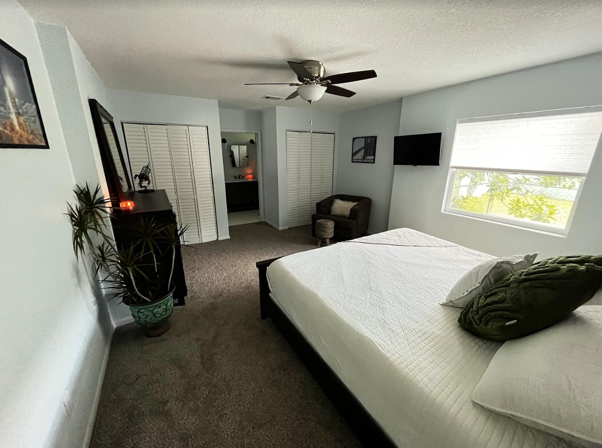 Bedroom with a queen bed, ceiling fan, wall-mounted TV, and large window with garden view