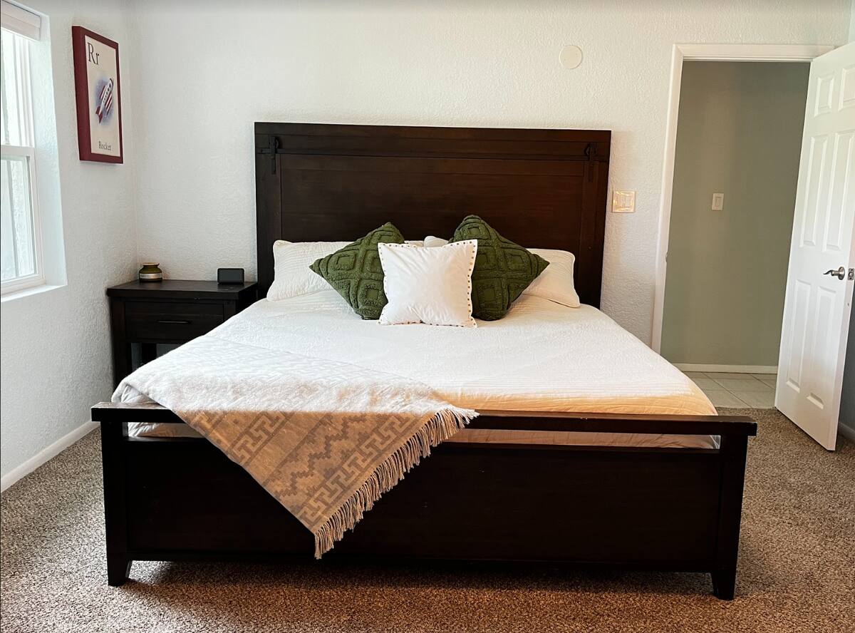Bedroom with a dark wood king bed, white bedding, green and white pillows, and a nightstand