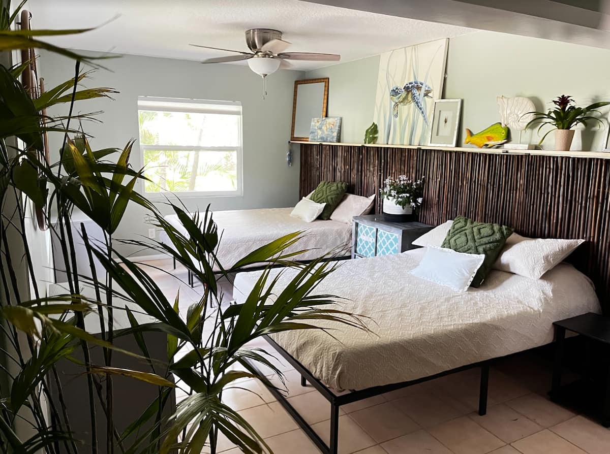 Bright bedroom with two beds, bamboo headboard, tropical decor, and green plants