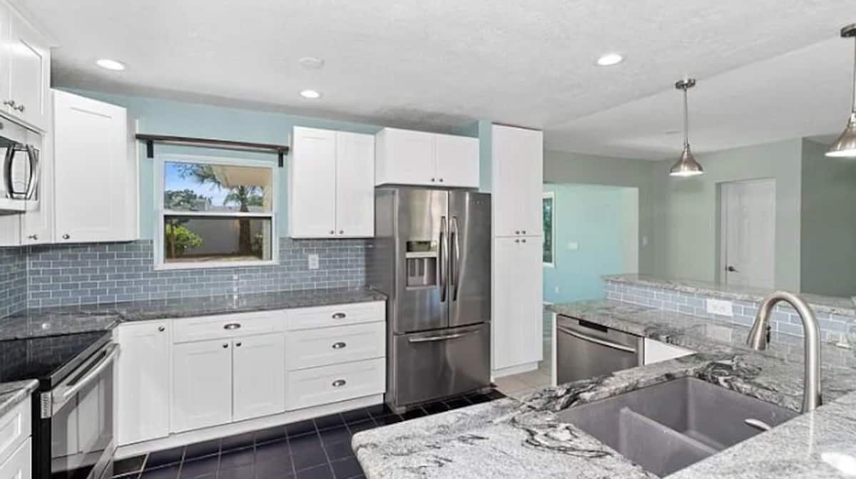 Renovated kitchen with white cabinets, granite countertops, stainless steel appliances, and blue tile backsplash