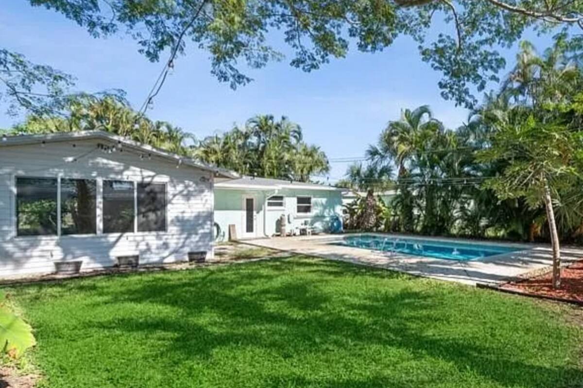 Backyard of a single-story rental home with an in-ground pool, green lawn, and tropical palm trees