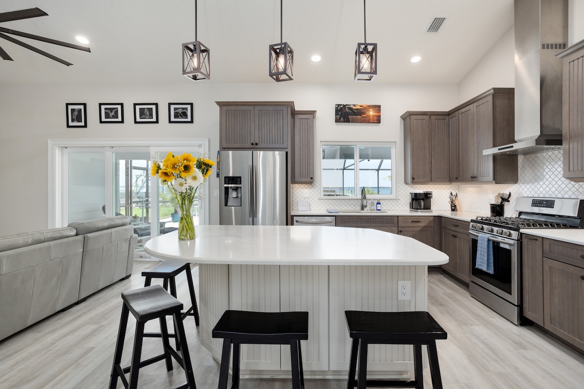 Open kitchen with large white quartz island, black stools and sliding doors to the waterfront patio